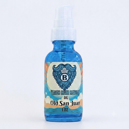 A 1 oz blue glass spray bottle of Beach Rum Remedy 'Old San Juan' oil, featuring a white pump and a colorful label with a blue bearded man's profile illustration.